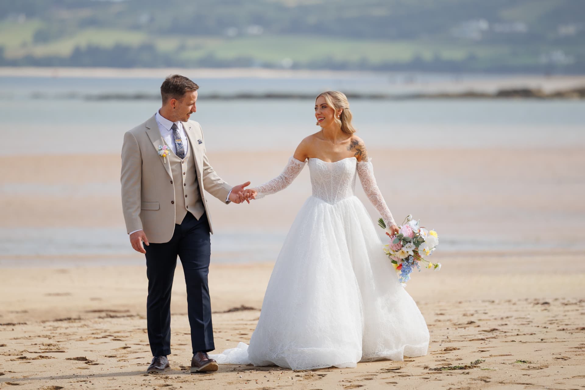 Bride and groom walking hand in hand along an Irish beach on their wedding day